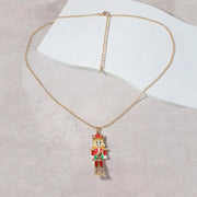 18K Gold Nutcracker Pendant Necklace on a marble surface, featuring a colorful Nutcracker charm and delicate gold chain.