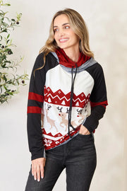 Smiling woman wearing a Double Take Christmas Hoodie with festive reindeer and snowflake patterns.
