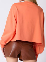 Back view of a woman wearing a cozy peach sweatshirt with long sleeves and brown shorts.