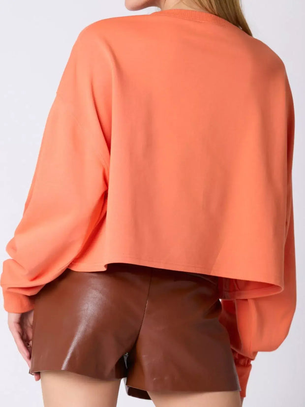 Back view of a woman wearing a cozy peach sweatshirt with long sleeves and brown shorts.