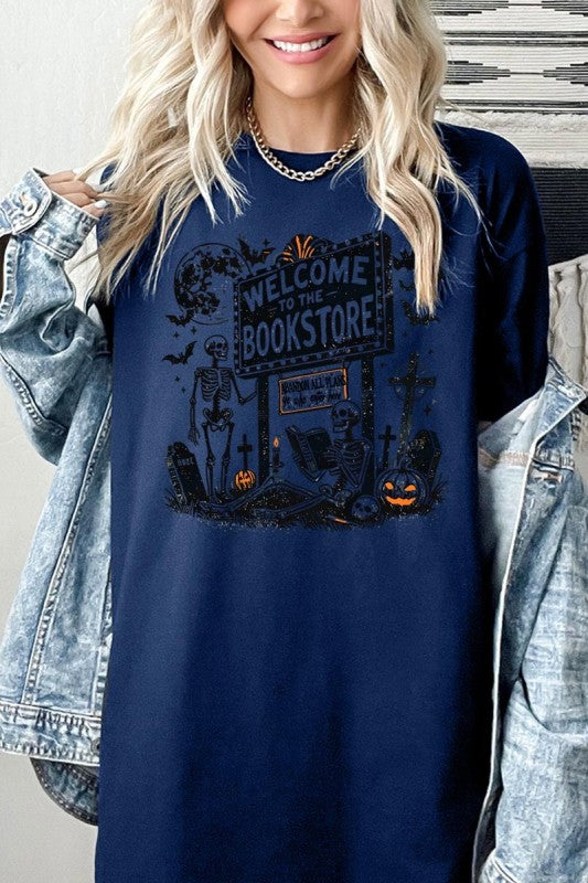 Bookstore Skeleton Halloween Graphic Heavy Cotton Tee worn by a smiling woman with a denim jacket.
