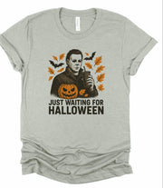 Just Waiting Halloween Graphic Tee featuring a spooky design with a pumpkin and fall leaves.