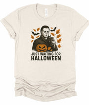 Just Waiting Halloween Graphic Tee featuring a spooky design with leaves, pumpkin, and a character holding a drink.