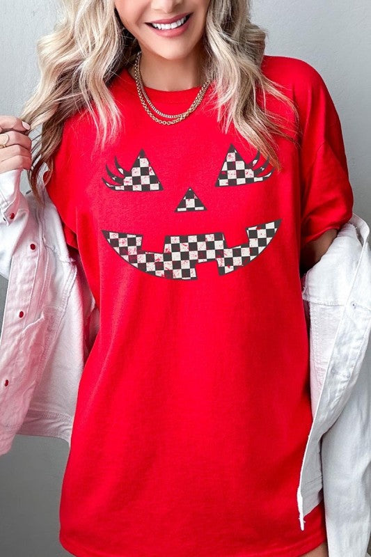 Checker Pumpkin Face Graphic Heavy Cotton Tee worn by a woman, featuring a checker pumpkin face design on a red background.