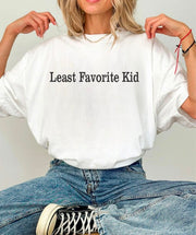 Woman wearing a Least Favorite Kid Short Sleeve Graphic Tee, showcasing a humorous graphic design.