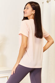 Model showcasing Simply Love Be Kind graphic tee in soft pink, emphasizing comfort and minimalist style.