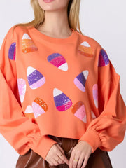 Halloween Candy Sequin Long-Sleeve Sweatshirt with colorful candy corn sequins on an orange background.