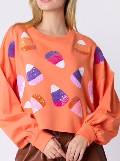 Halloween Candy Sequin Long-Sleeve Sweatshirt with colorful candy corn sequins on an orange background.