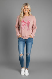 Model wearing Bow Graphic Round Neck Long Sleeve Sweatshirt with a pink bow graphic, paired with distressed jeans.