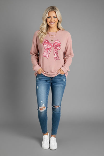 Model wearing Bow Graphic Round Neck Long Sleeve Sweatshirt with a pink bow graphic, paired with distressed jeans.