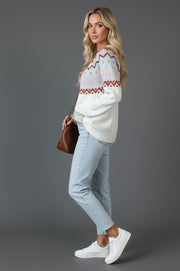 A side view of a model wearing a Cozy Geometric Knit Round Neck Sweater, paired with light blue jeans and white sneakers, posing with a brown handbag.