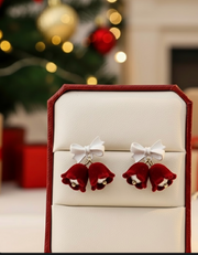 Velvet Bell Earrings with Bow displayed on a jewelry stand with holiday decorations in the background.