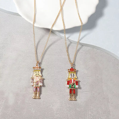 18K Gold Nutcracker Pendant Necklace displayed on a plate, featuring two colorful Nutcracker charms.