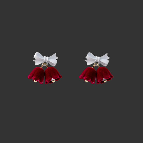 Velvet Bell Earrings with Bow displayed on a jewelry stand with holiday decorations in the background.