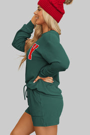 Woman wearing Evergreen MERRY Corded Lounge Set in cozy setting with Christmas tree, showcasing festive style and comfort.